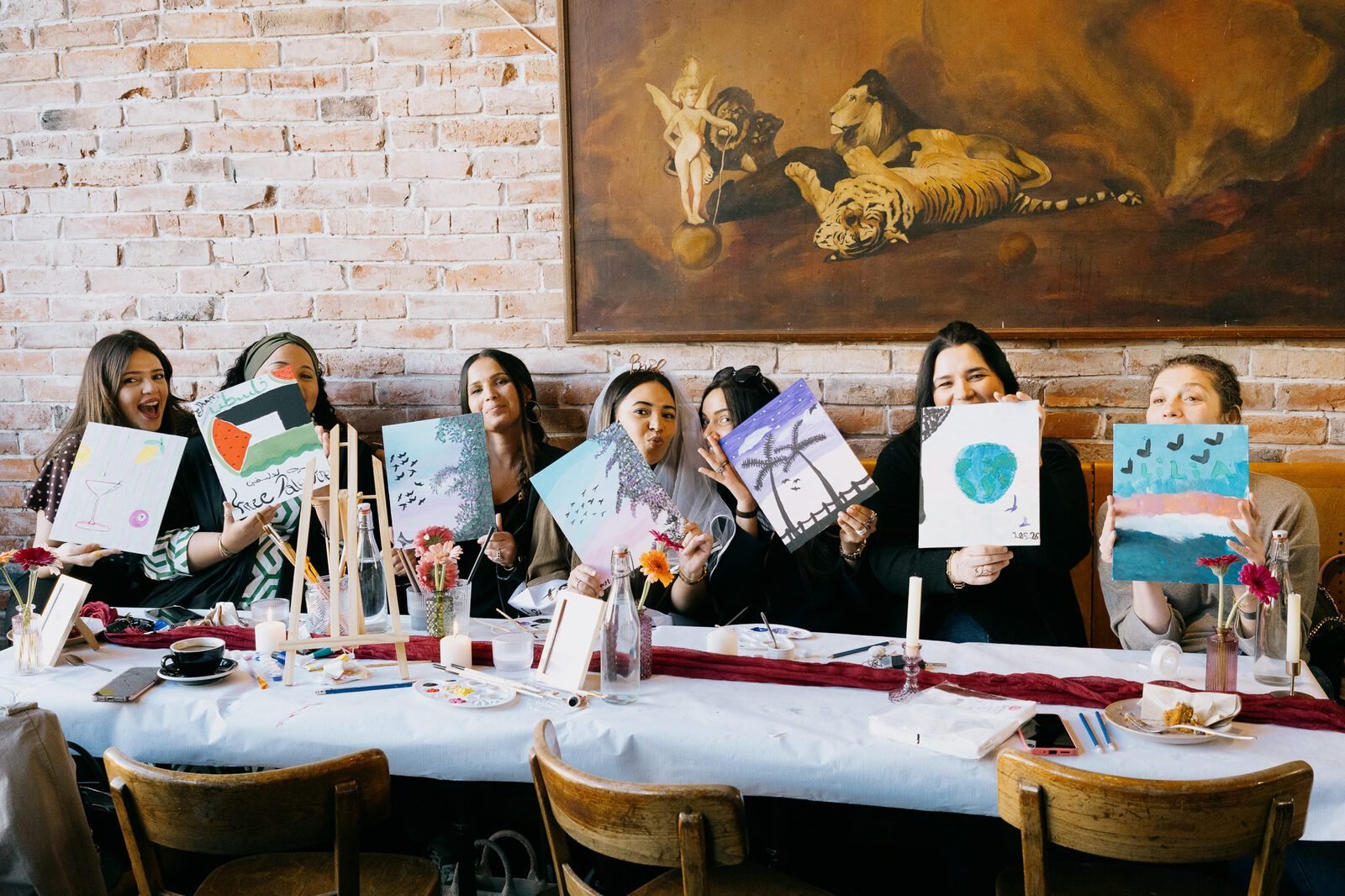 Les participantes d'un atelier alignées derrière la table, présentant chacune la toile qu'elle vient de peindre