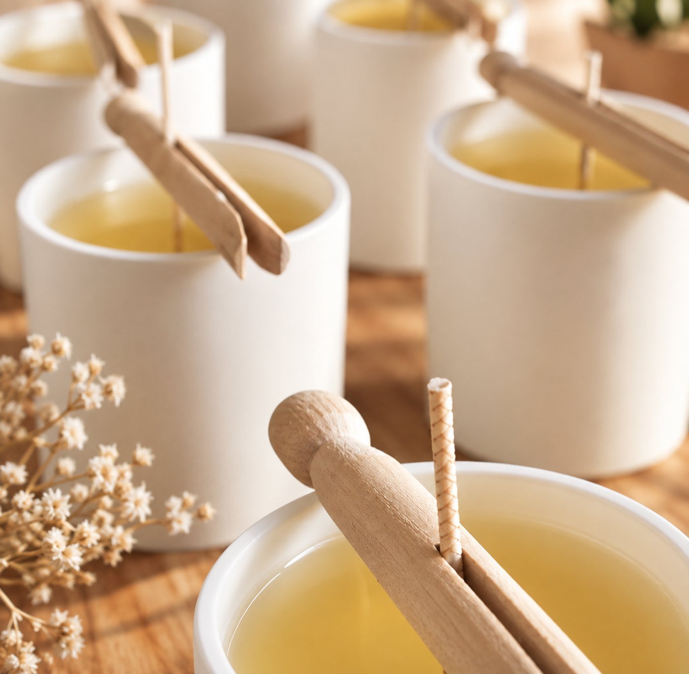 Contenants en céramique blanche et mèches maintenues par des bâtonnets en bois, prêts pour un atelier de création de bougies