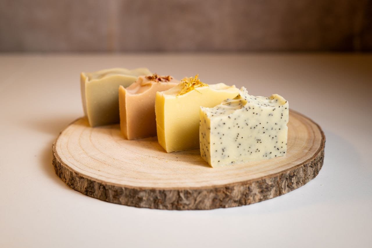 Quatre savons naturels faits main posés sur une rondelle de bois, atelier With Nürya à Genève
